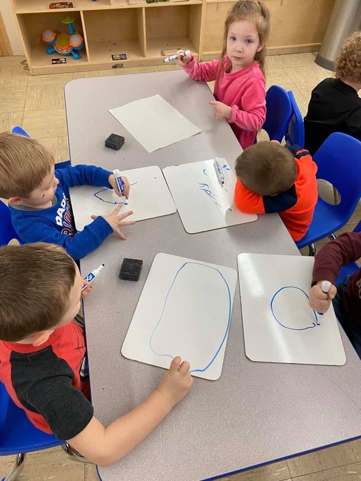 Children drawing on whiteboards at a table in a classroom