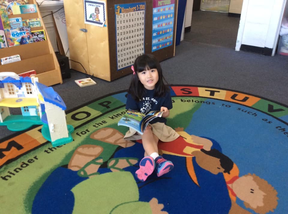 Child sitting on a rug and reading a book in a classroom