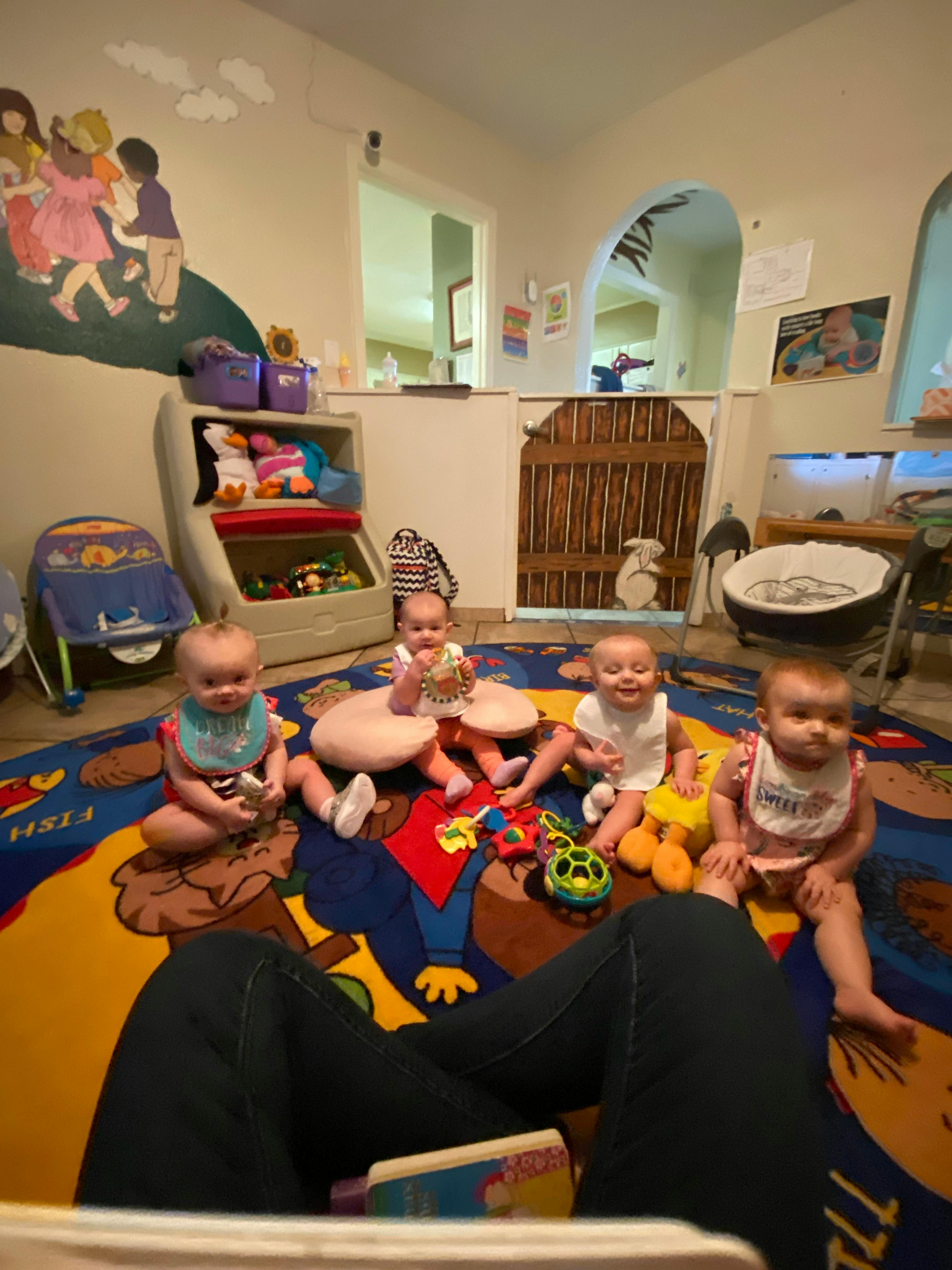 Four babies sitting on a colorful rug with toys