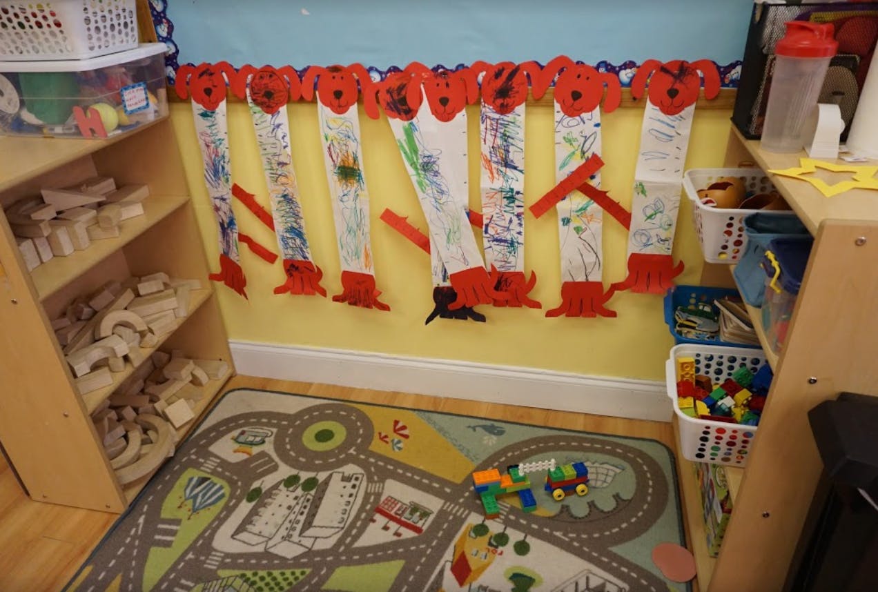Classroom with a play rug, shelves, and children's artwork on the wall