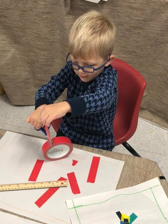 Child cutting red tape with scissors at a table