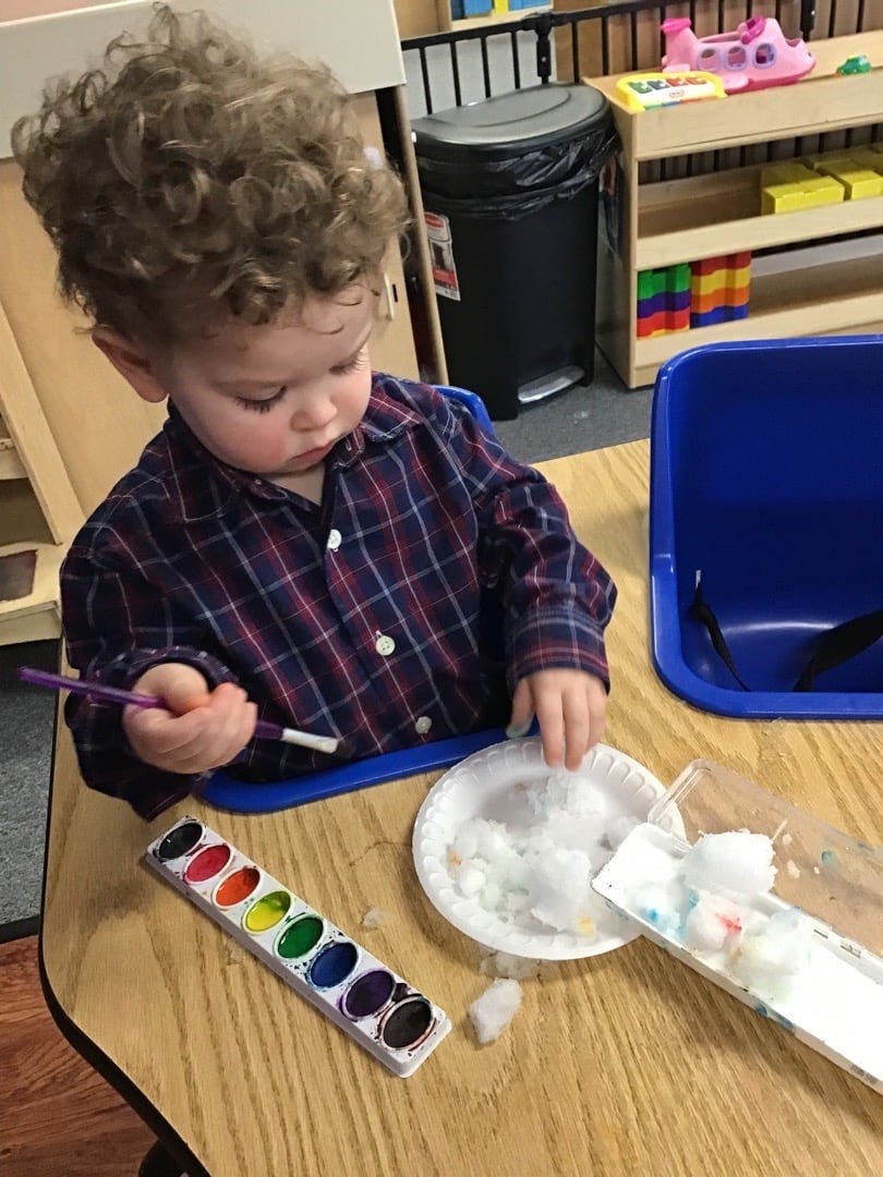 Child painting cotton balls with watercolors in a classroom