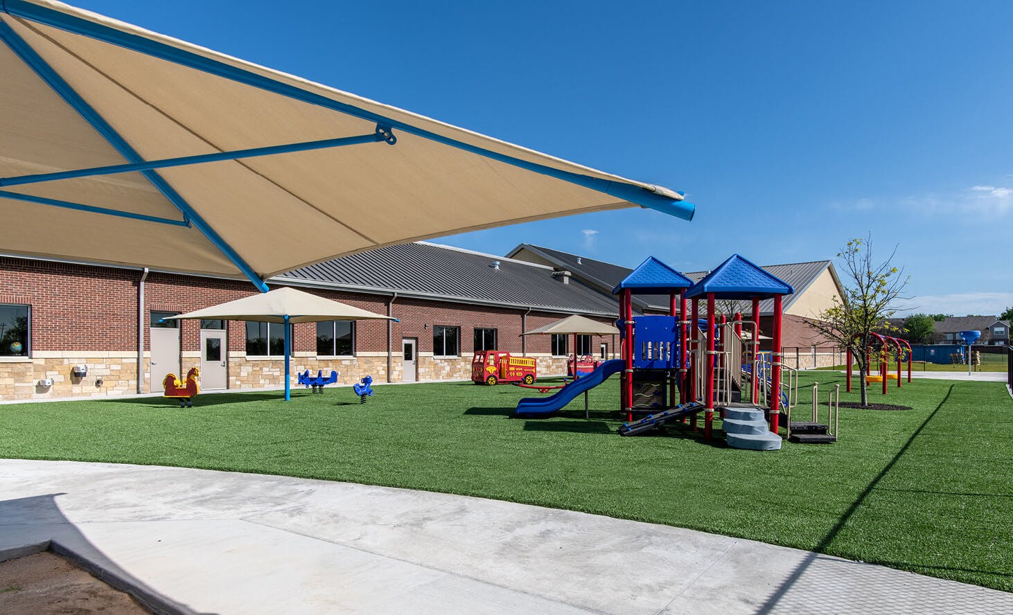 Outdoor playground with artificial turf, play structures, and shade sails