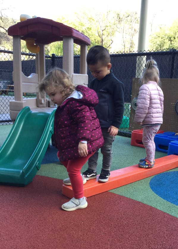 Three children playing on a balance beam and slide on a playground
