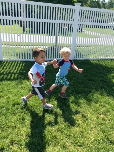 Two children running on grass, holding hands