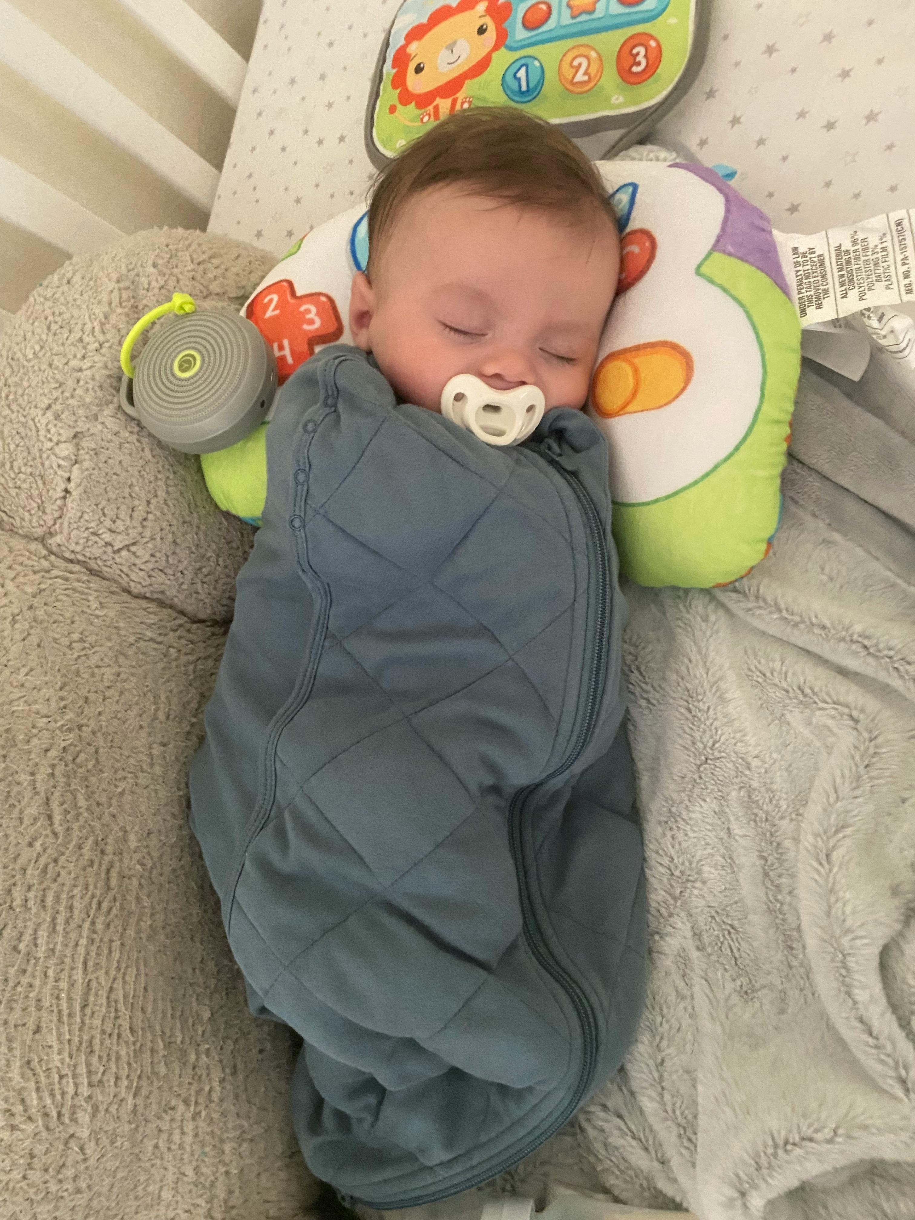 Sleeping baby in a blue sleep sack with a pacifier in their mouth