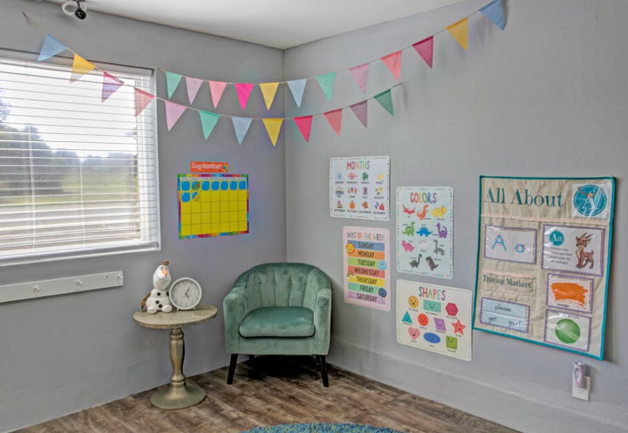 Corner of a room with a green chair, small table, and educational posters