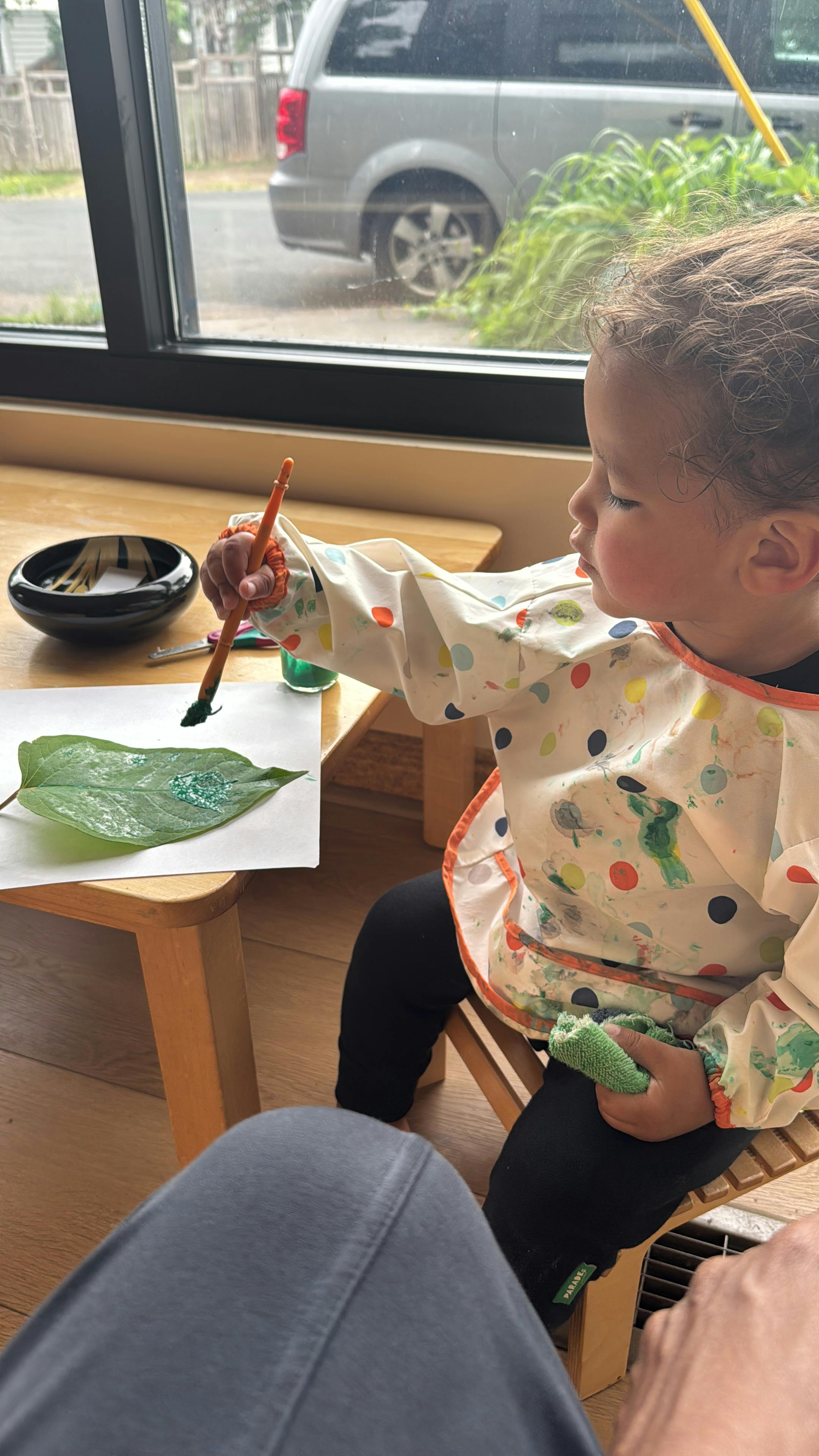 Child in a smock painting on a large green leaf with a paintbrush