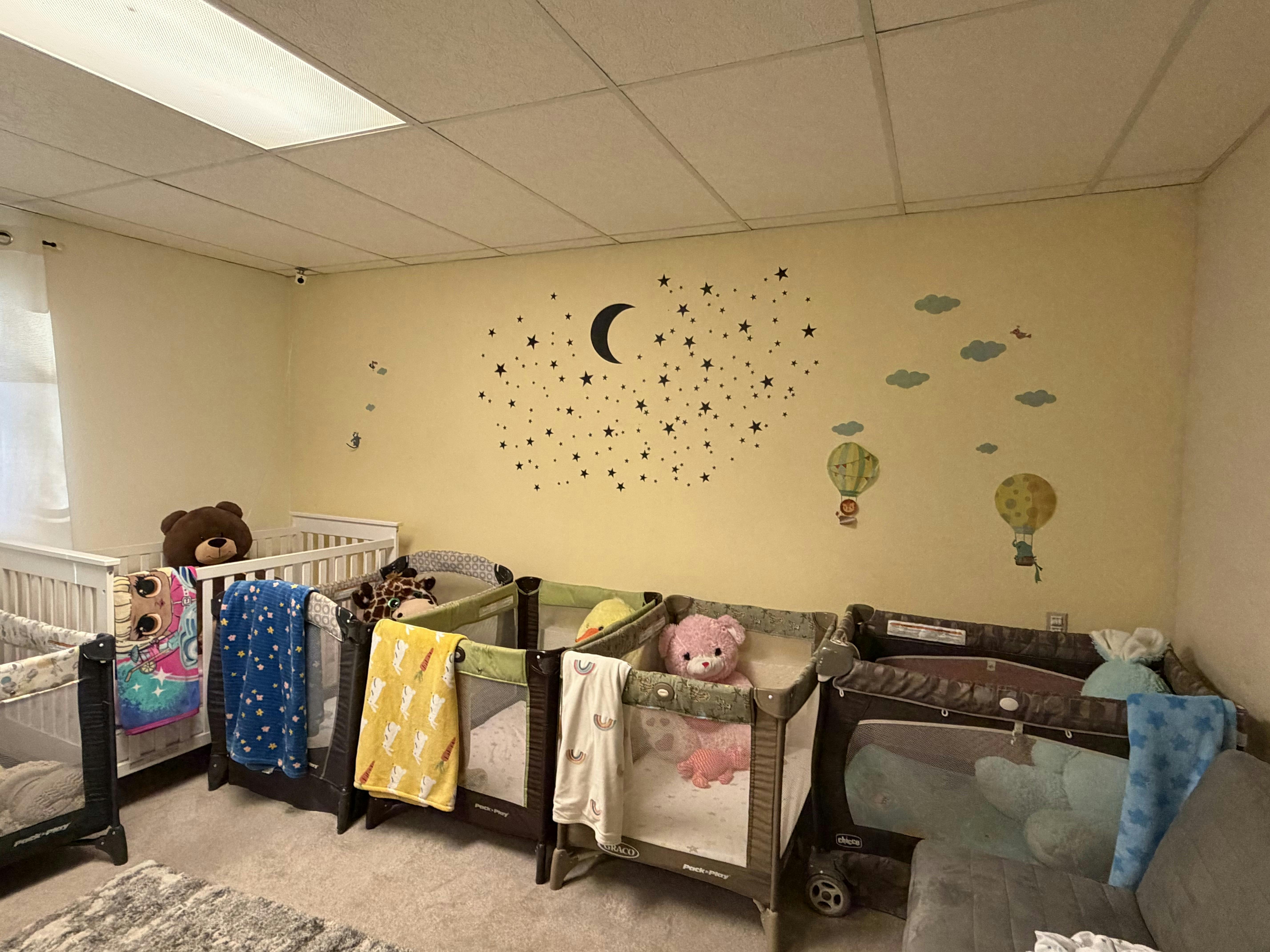 Multiple cribs in a room with wall decals of moon and stars decals