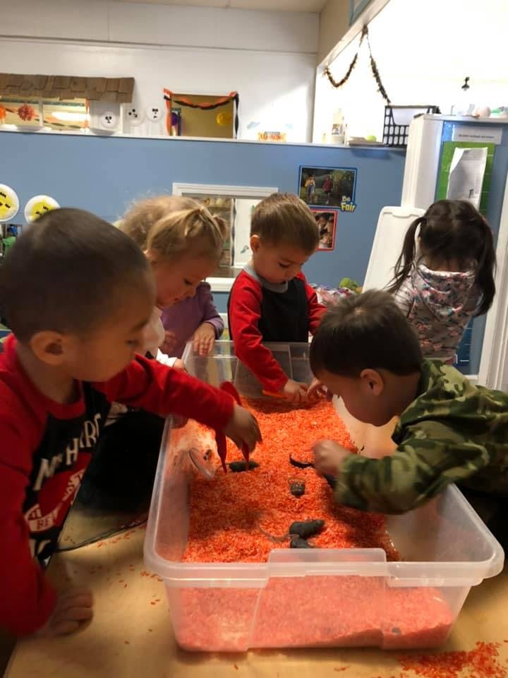 Children playing with orange sensory bin filler and small objects