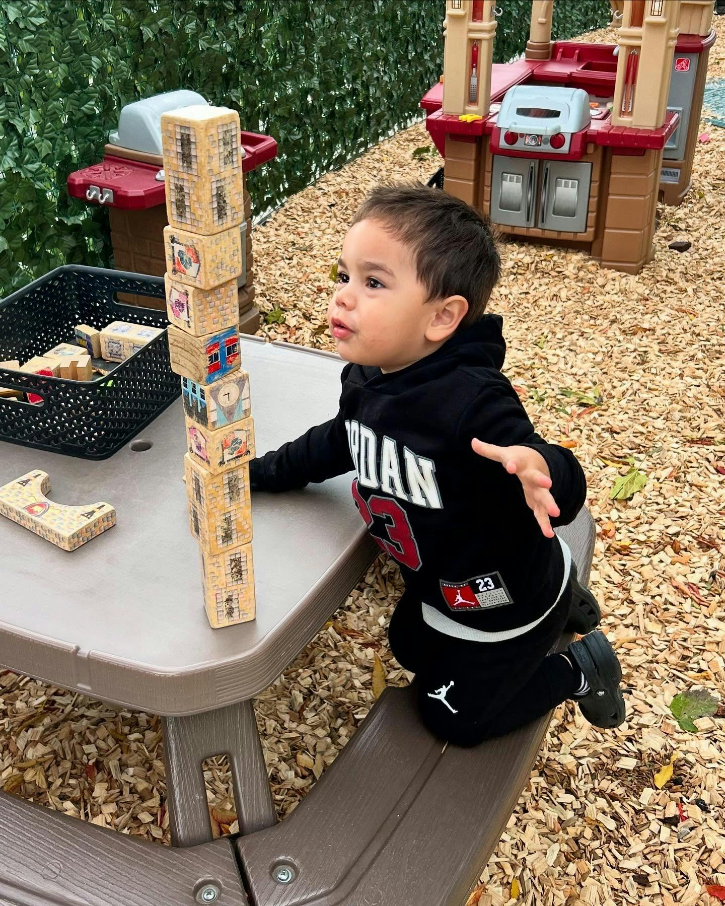 Child kneeling on a bench while stacking wooden blocks on a table