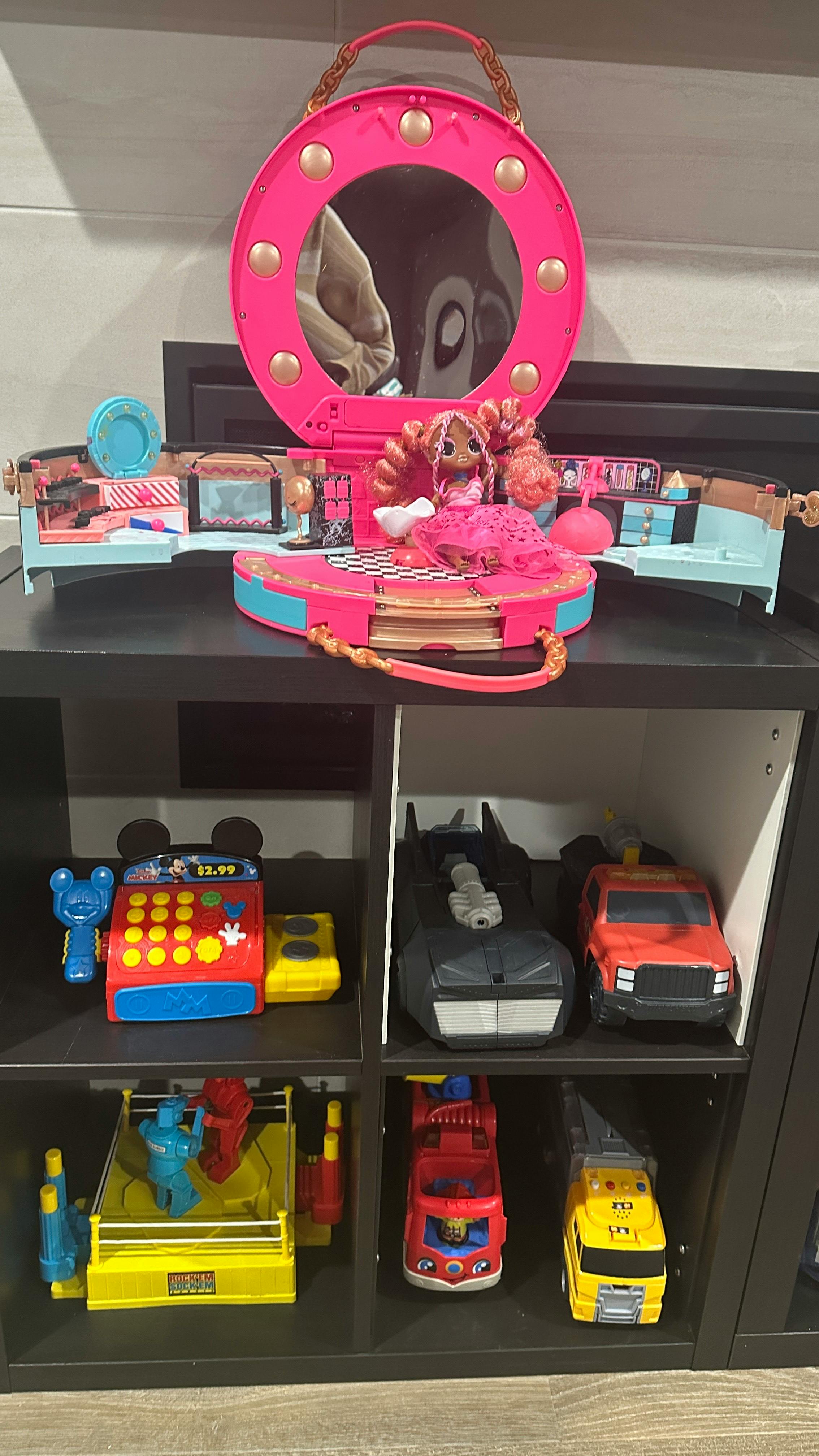 Shelf with various toys including a doll, toy cars, and a cash register