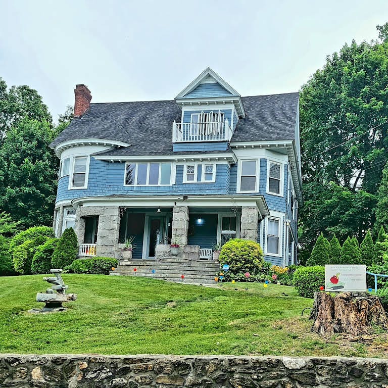 Large blue house with a dark roof and stone foundation on the lower level