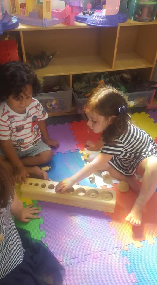 Two children playing with a wooden puzzle on a colorful mat
