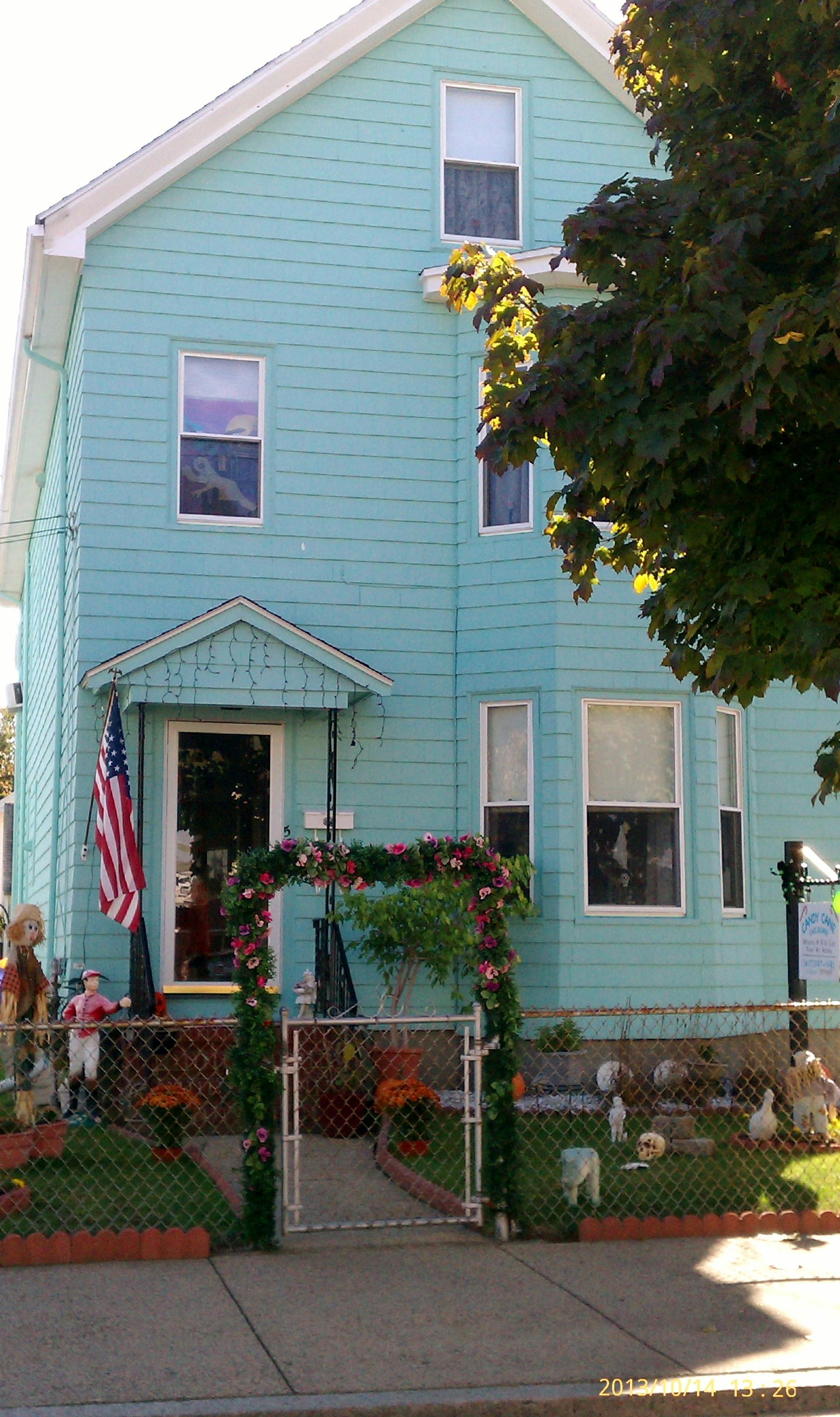 Light blue house with an American flag and a floral archway over a gate