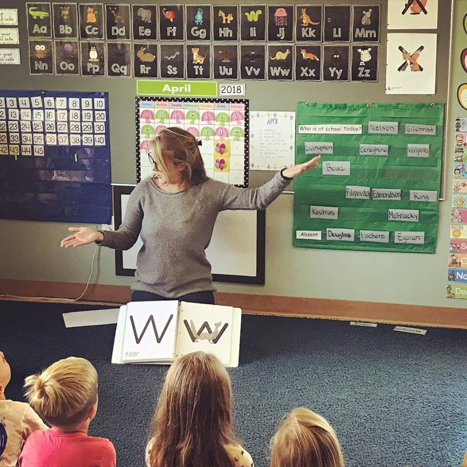 Person teaching children in a classroom with a large letter W on display