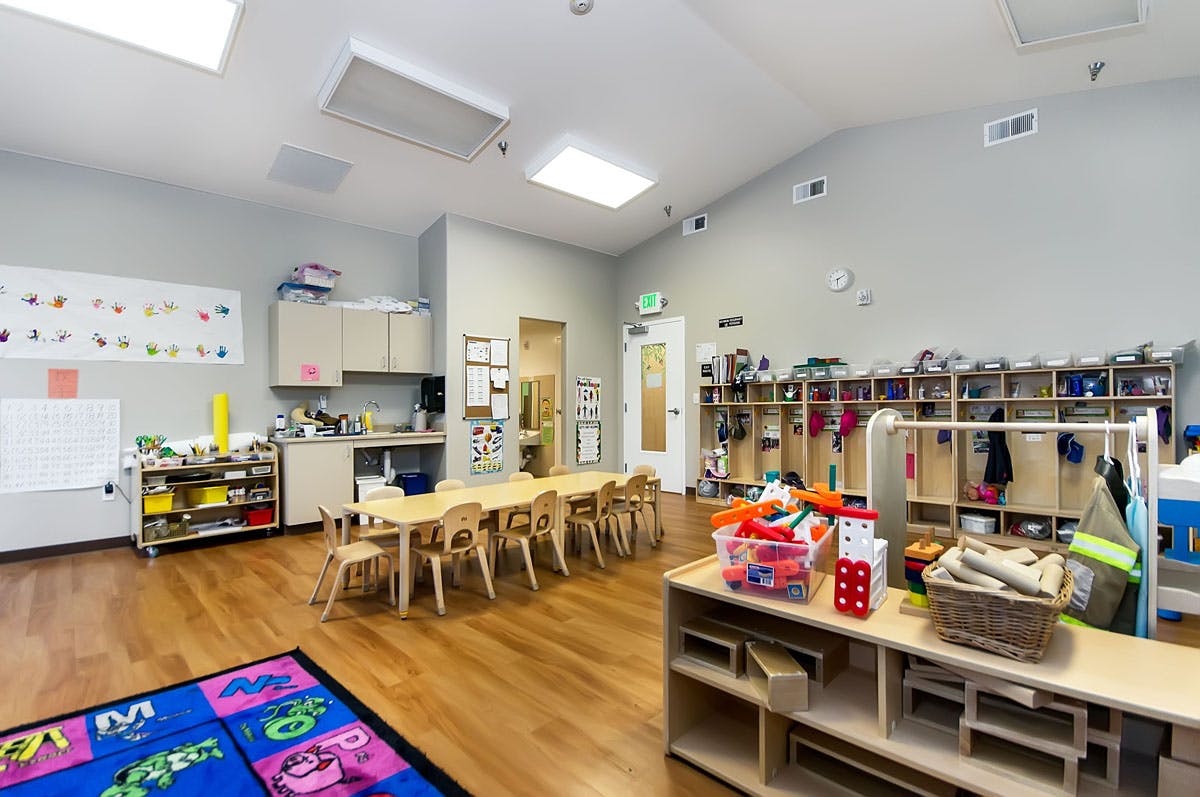Empty classroom with small tables and chairs, storage cubbies, and a play rug