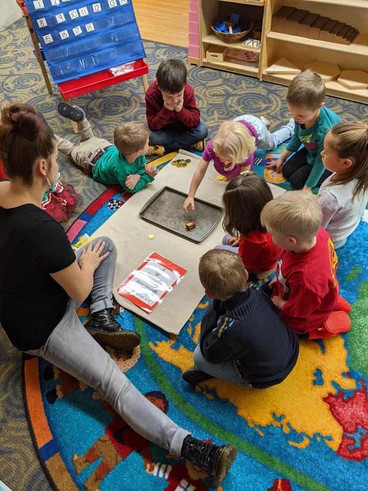 Adult and children sitting on a rug, looking at an object on a tray