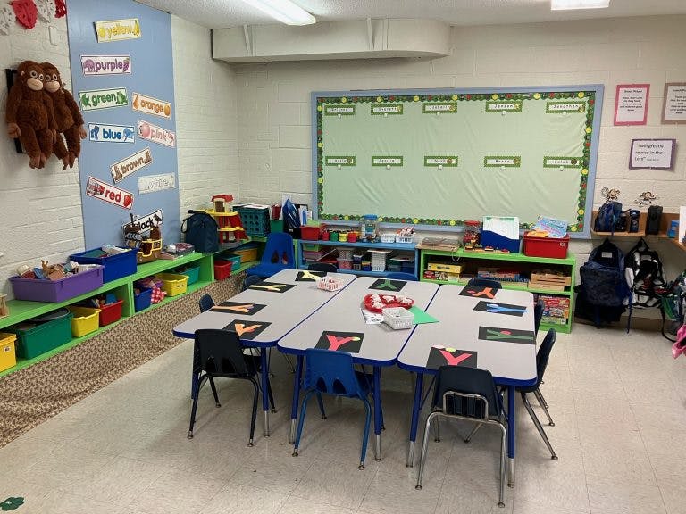 Classroom with tables and chairs, shelves with supplies, and a bulletin board