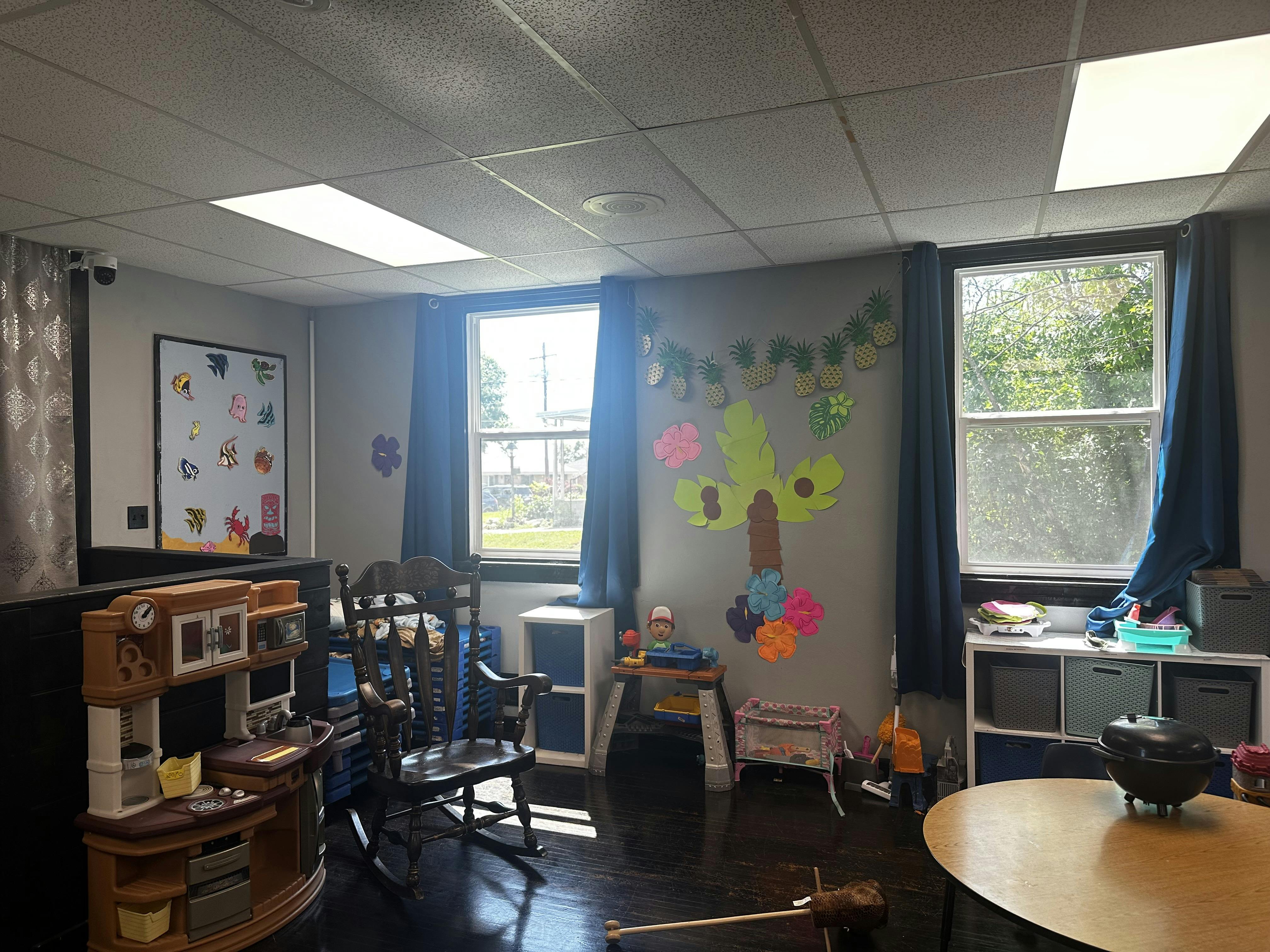 A classroom with windows, a rocking chair, and children's play furniture