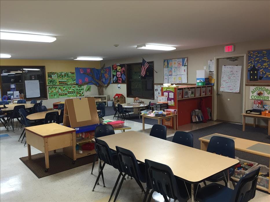 Empty classroom with small tables and chairs, children's artwork on walls