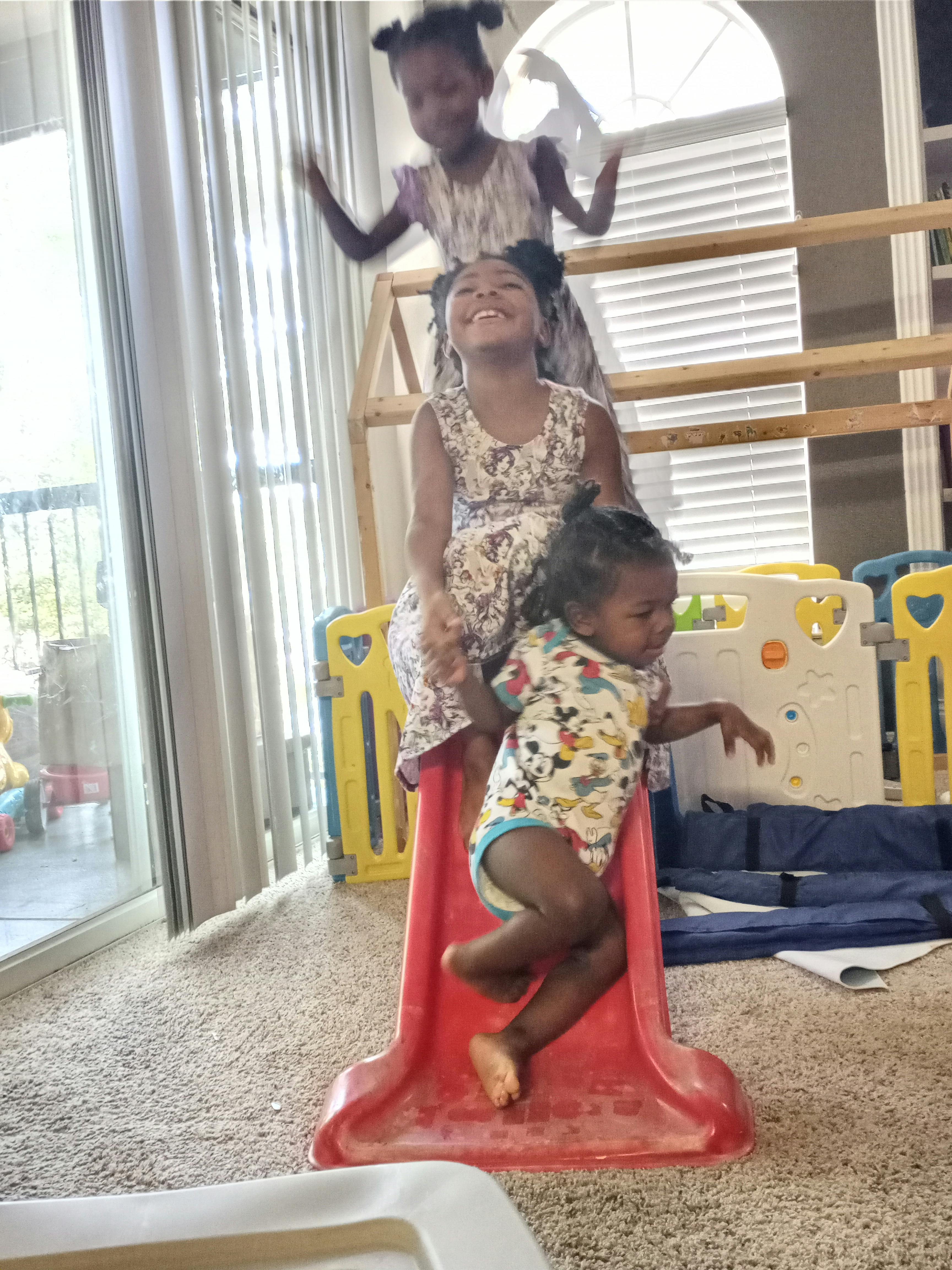 Three children playing on a small red slide indoors