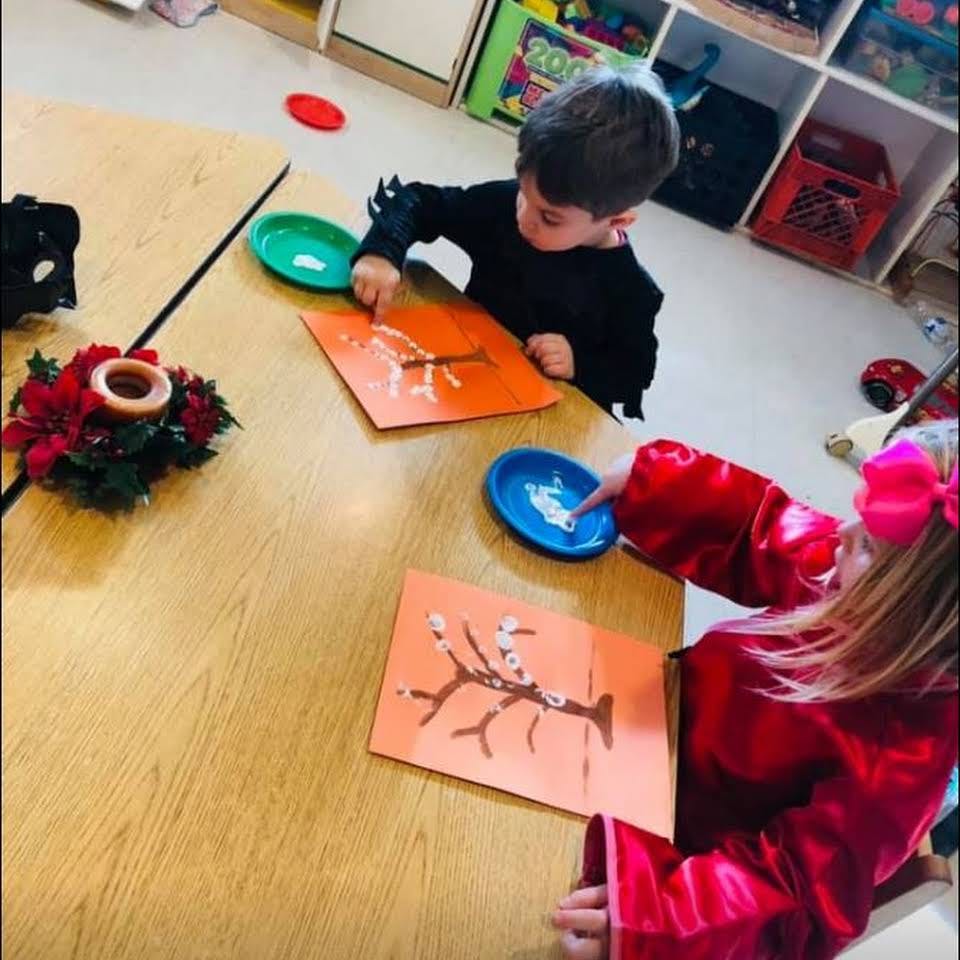 Two children painting tree branches on orange paper