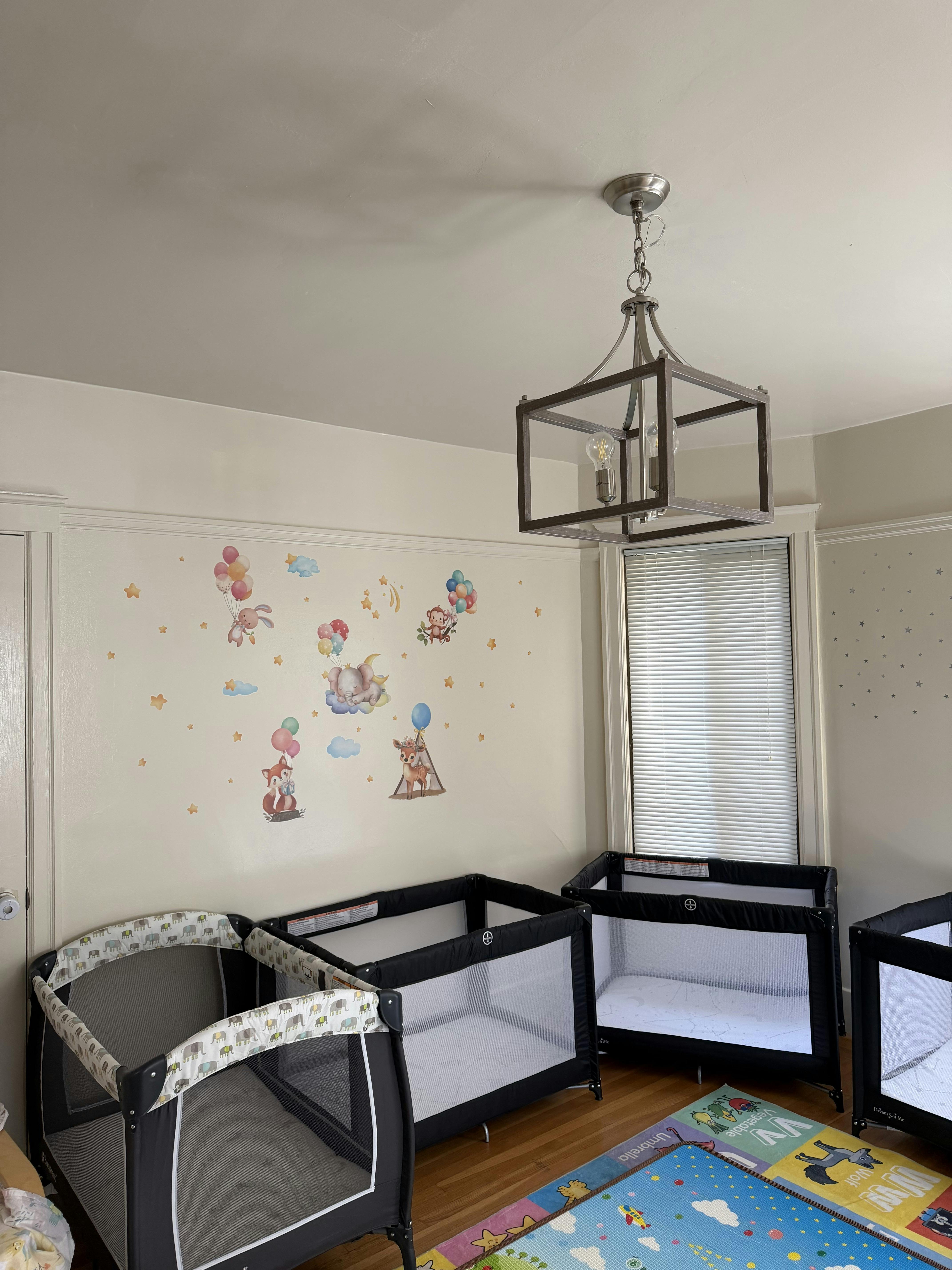 A room with several portable cribs and animal-themed wall decals