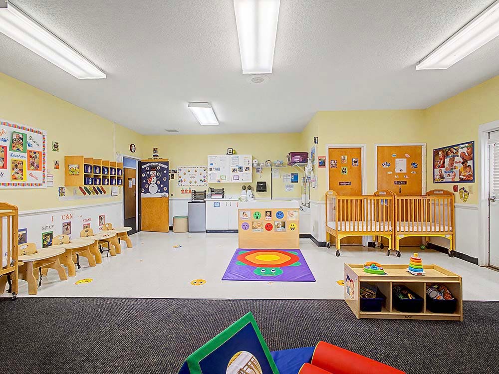 A colorful childcare classroom with cribs, small tables, and learning decorations