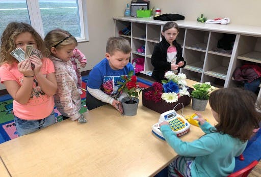 Children playing with toy money, flowers, and a cash register