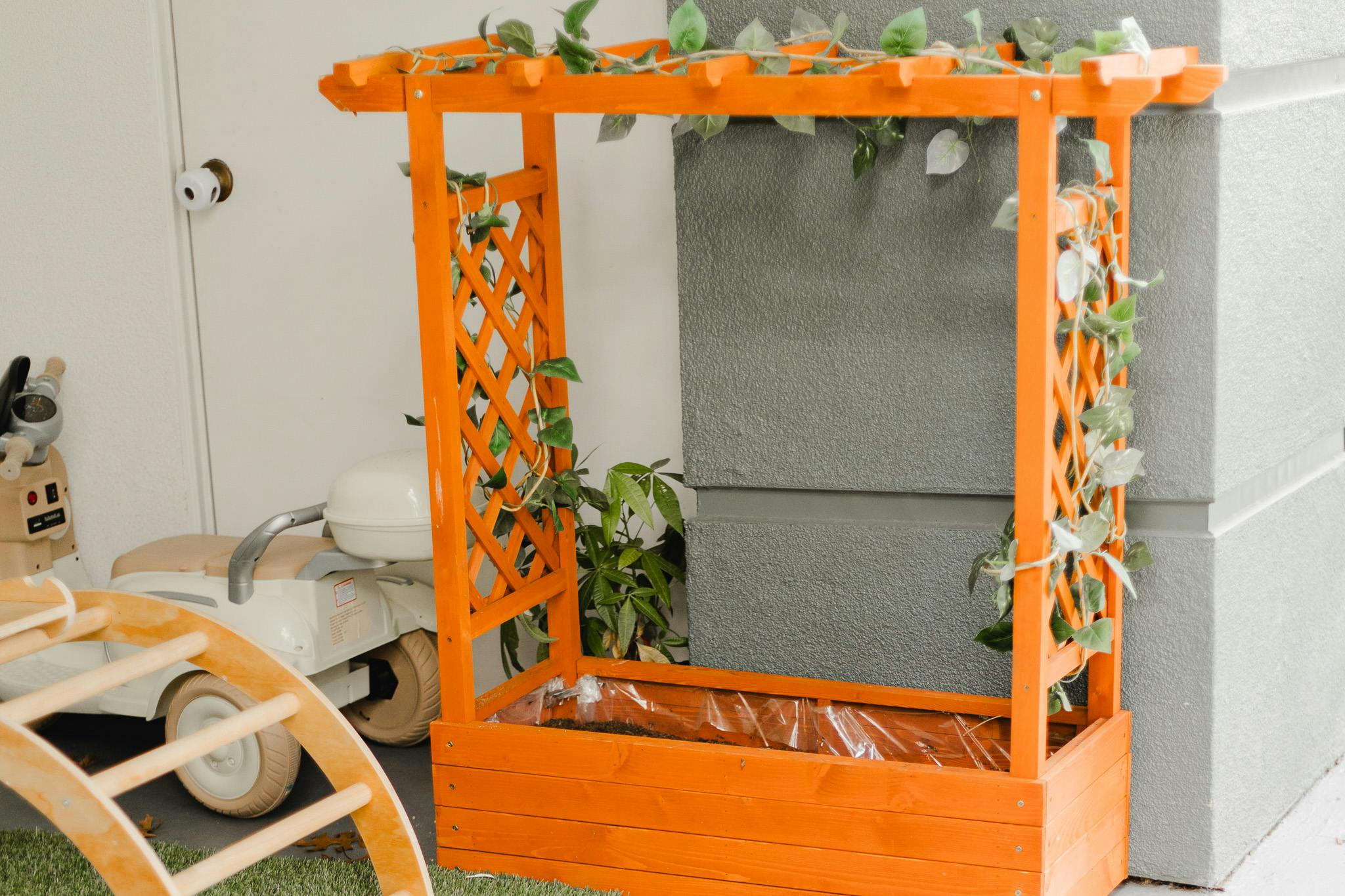 Orange wooden planter box with a trellis and artificial vines
