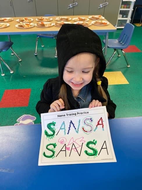 Child in a classroom holding a name tracing practice sheet