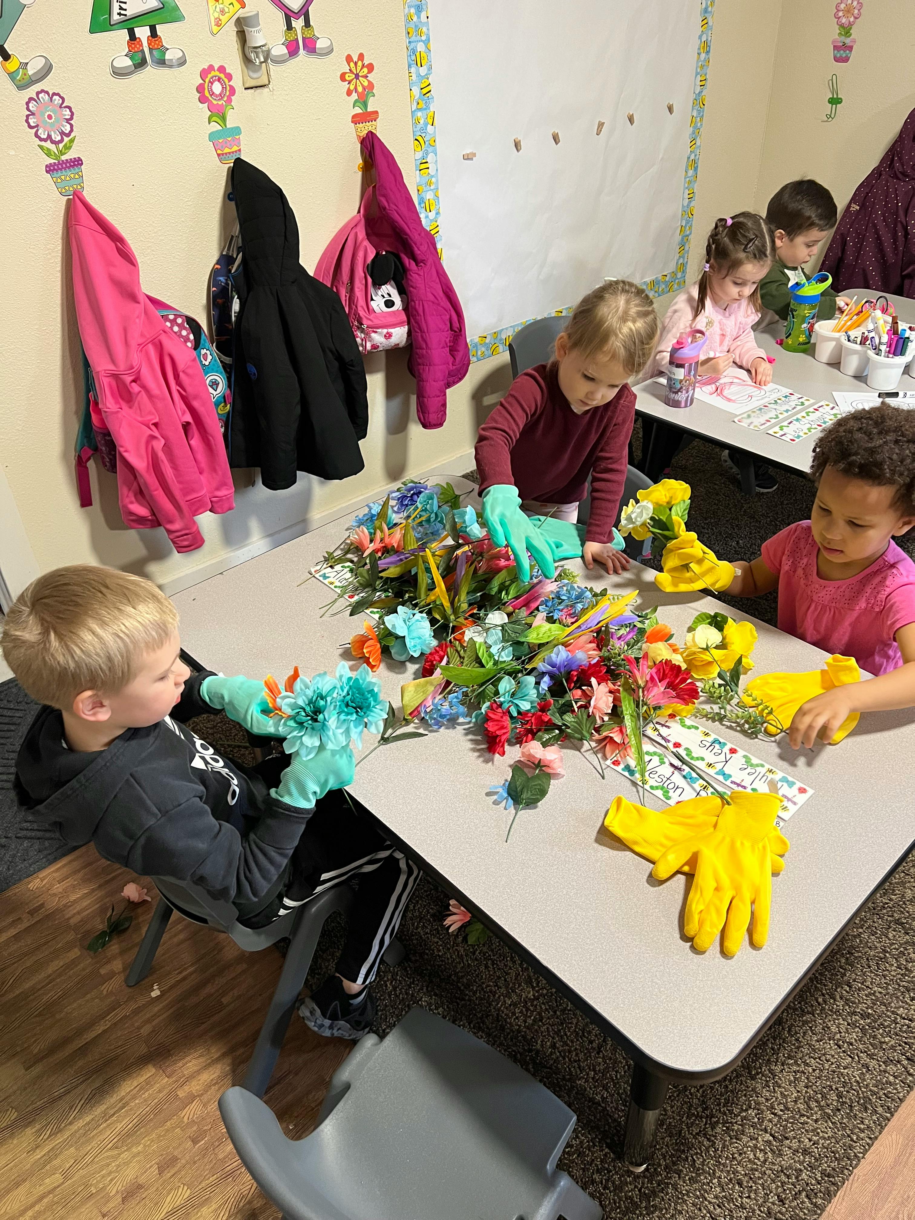 Children wearing gloves and playing with artificial flowers at a table