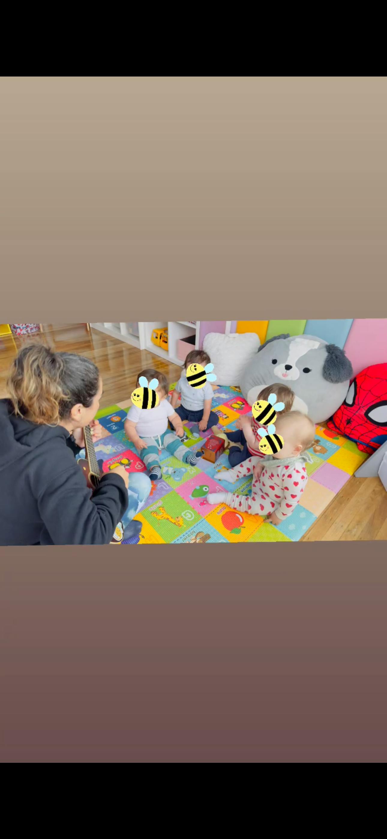 Person playing a ukulele for a group of children sitting on a colorful floor mat