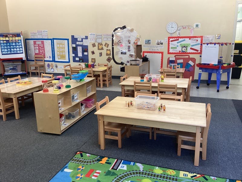 Empty classroom with small tables, chairs, and shelves with toys