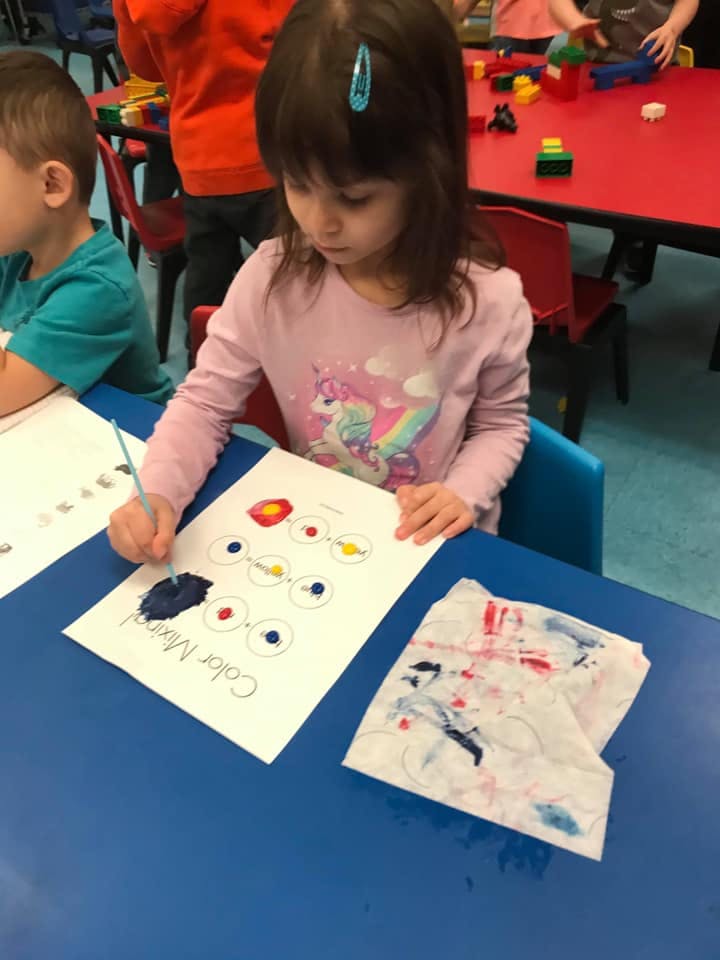 Child painting on a paper with "Color Mixing" written on it