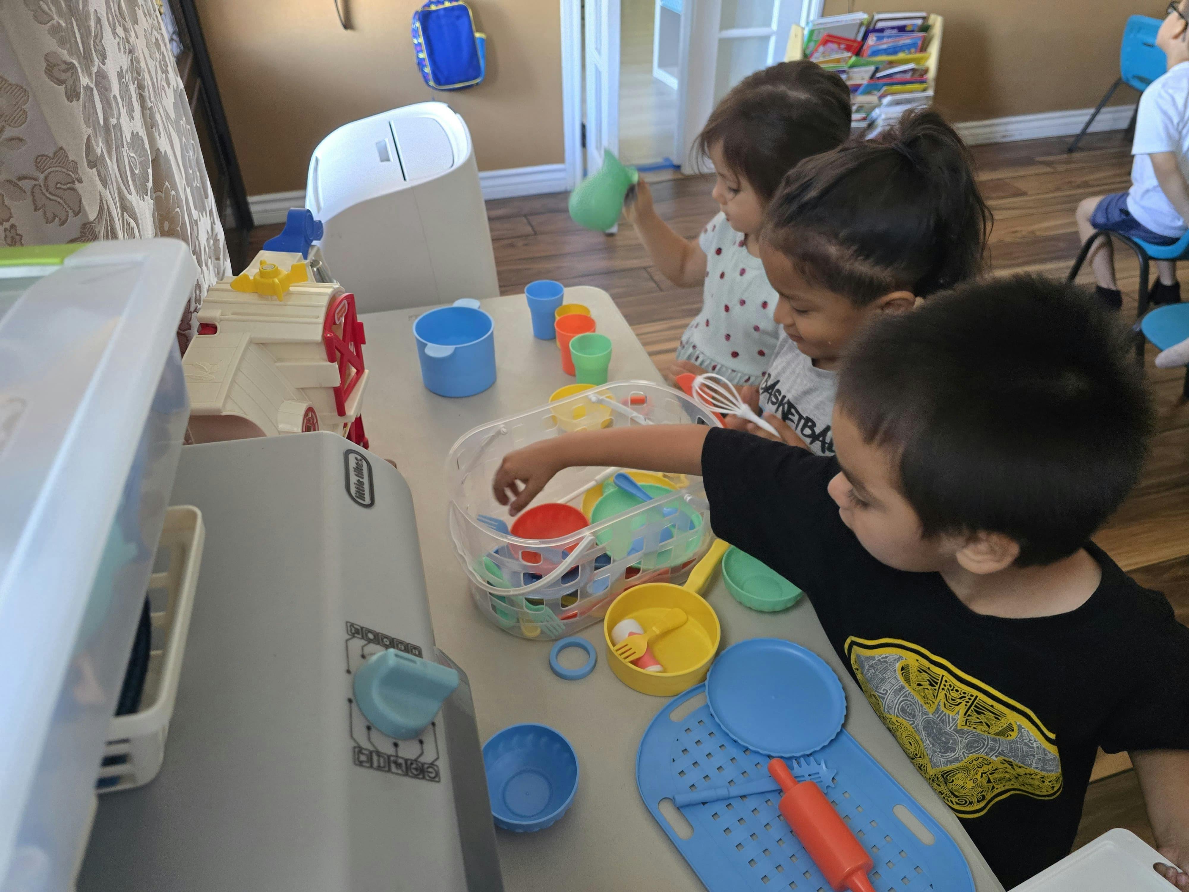 Three children playing with plastic toy kitchenware at a table