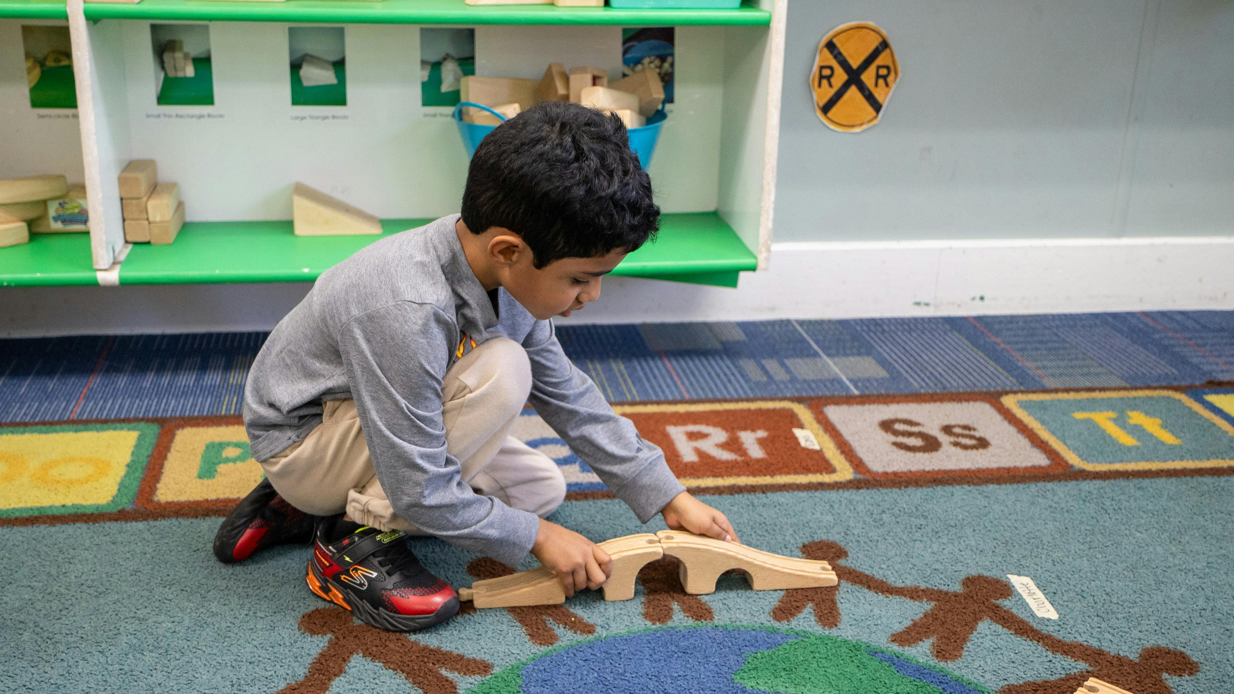 Child playing with wooden toy bridge on a rug