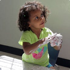 Child with curly hair playing with white modeling clay