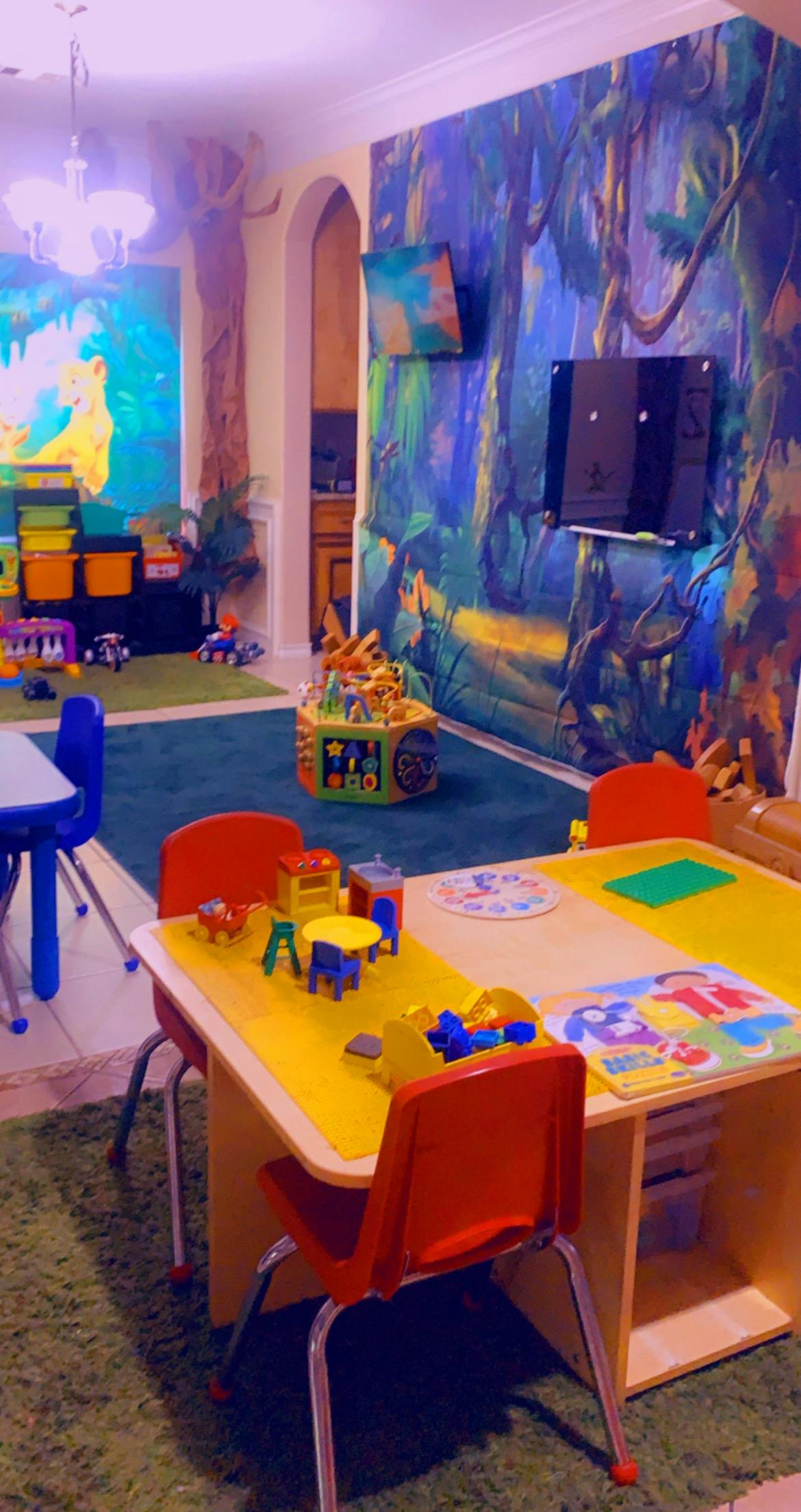 Playroom with small tables and chairs, toys, and jungle-themed wall murals
