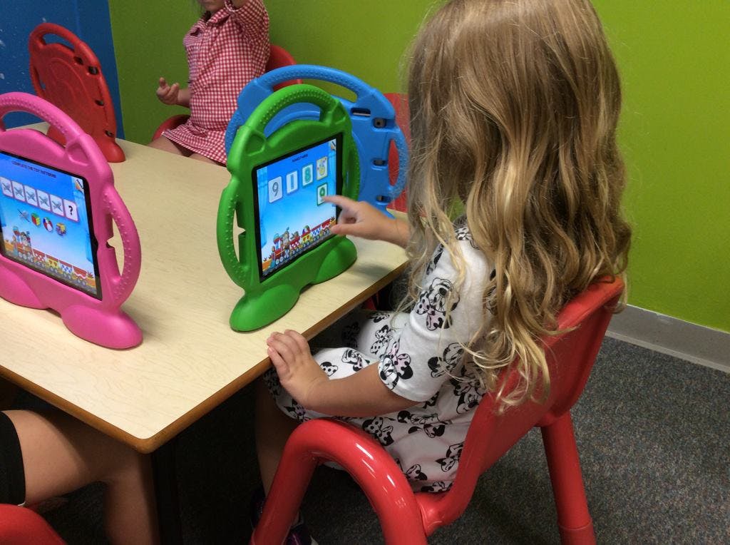 Child sitting at a table using a tablet in a green protective case