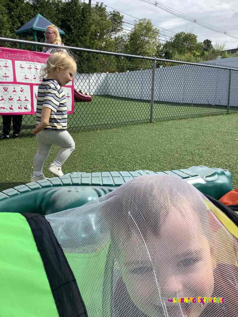 Child in striped shirt walking past another child in a play tunnel