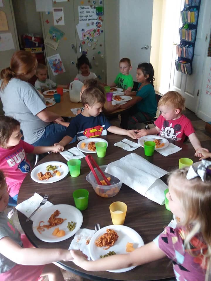 Adult and children holding hands around a table with plates of food