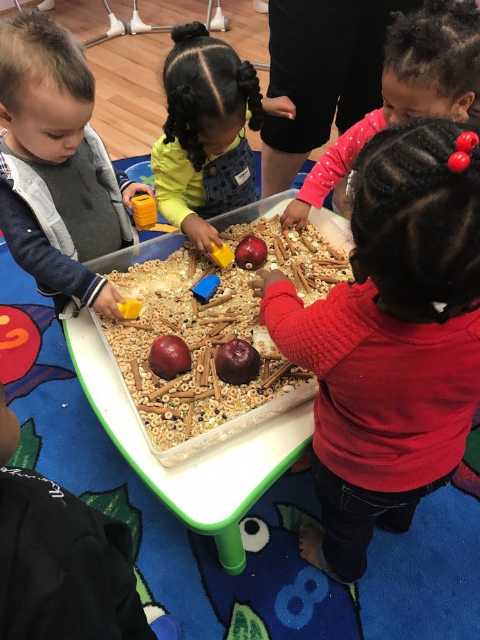 Children playing with a sensory bin filled with cereal and apples