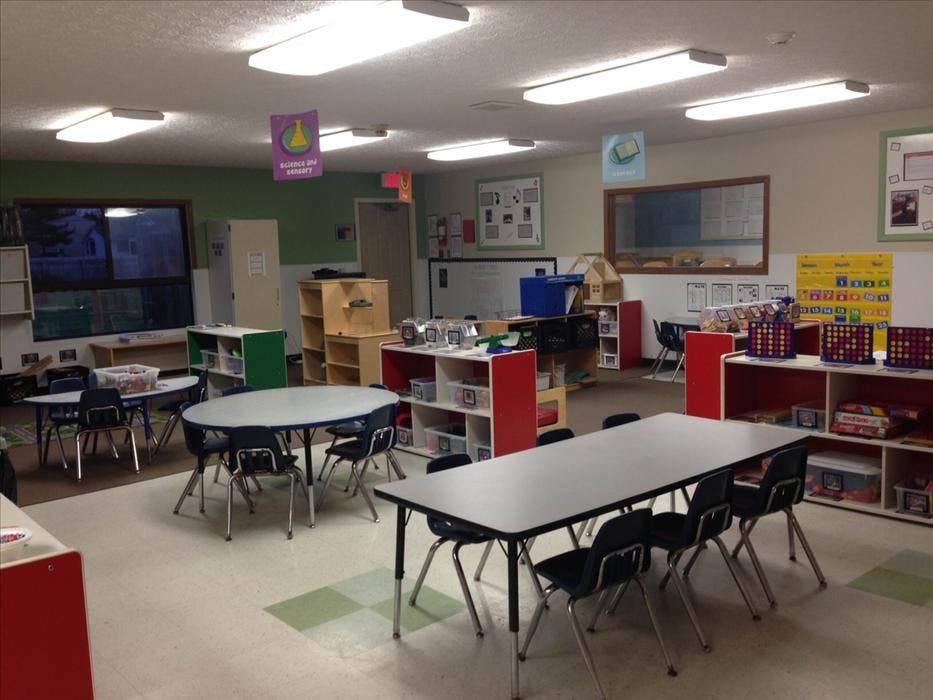 An empty classroom with multiple tables, chairs, and learning materials
