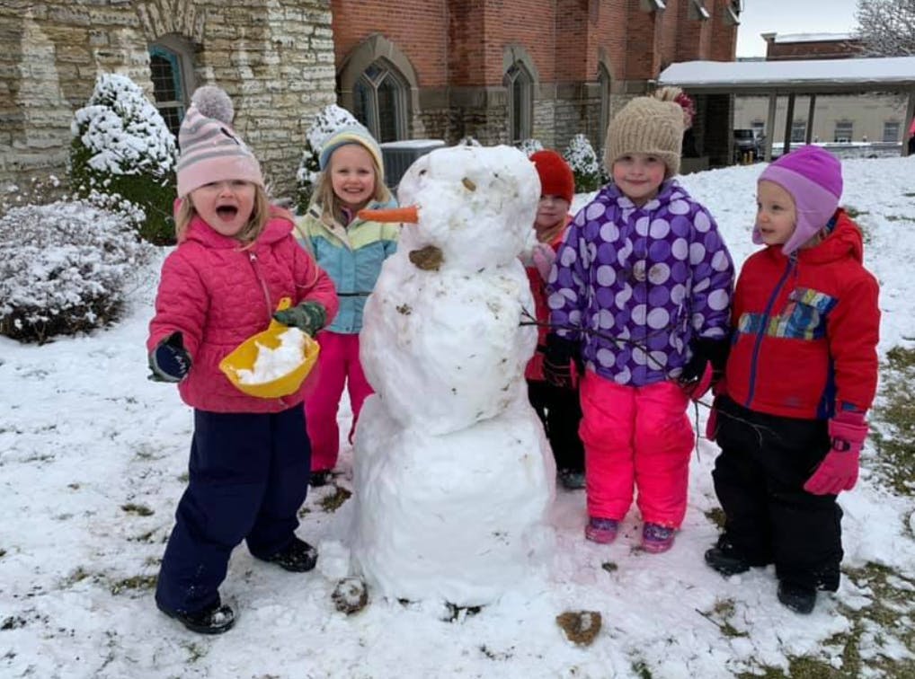 Children standing around a snowman in the snow