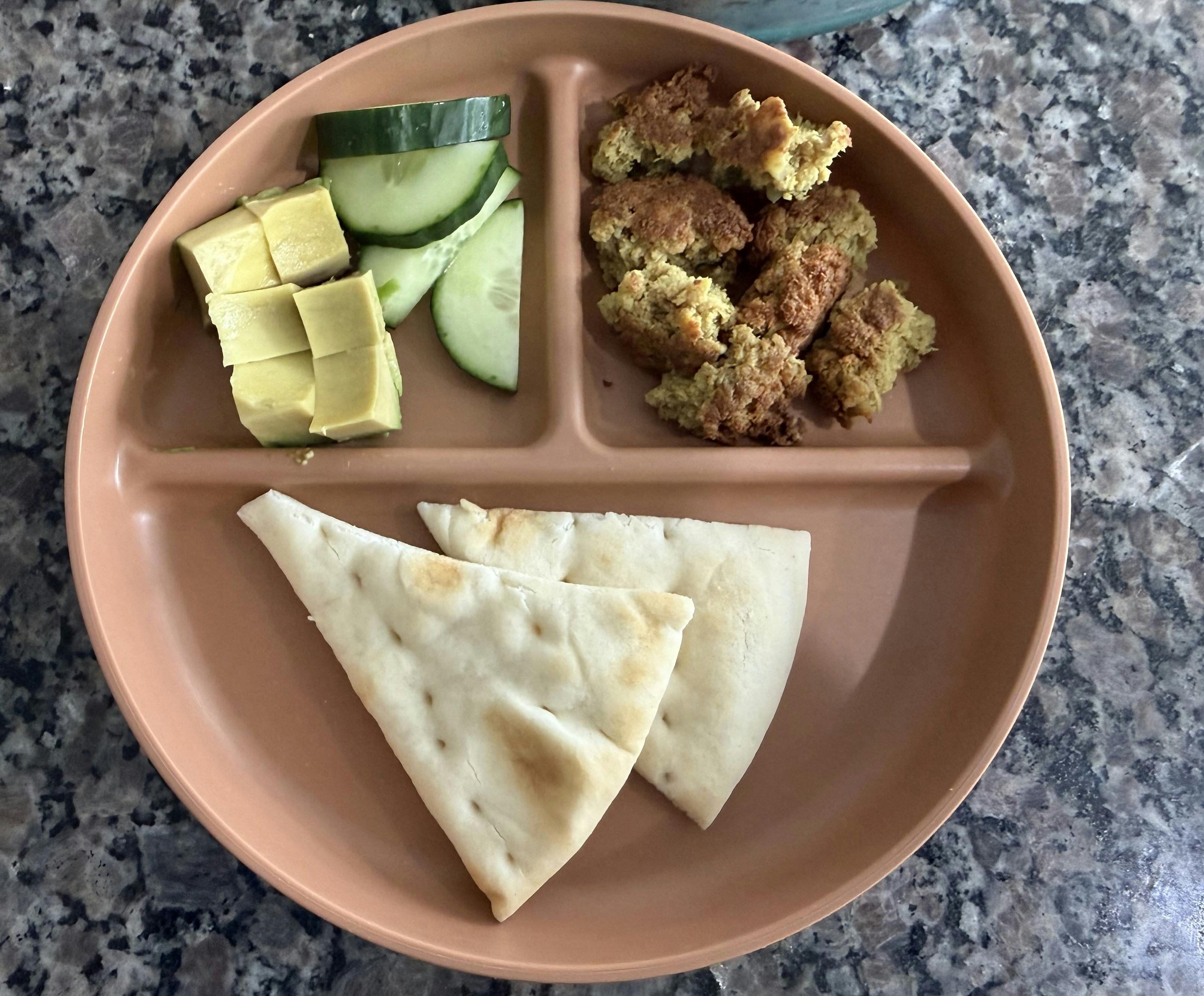 Falafel, pita bread, sliced cucumbers, and avocado on a plate