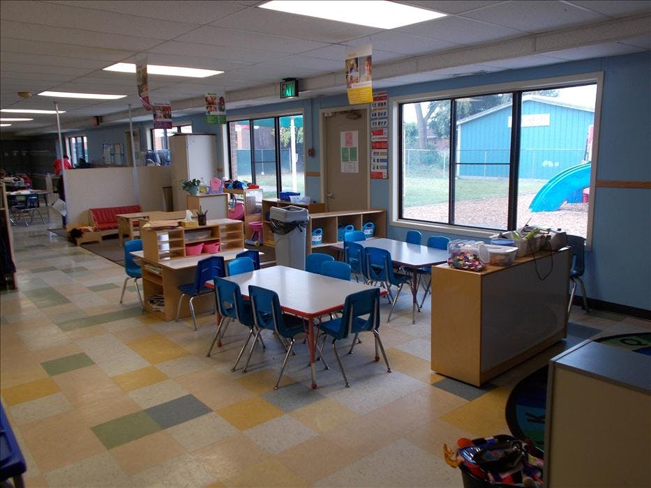 Classroom with multiple tables and chairs, and a window overlooking a playground