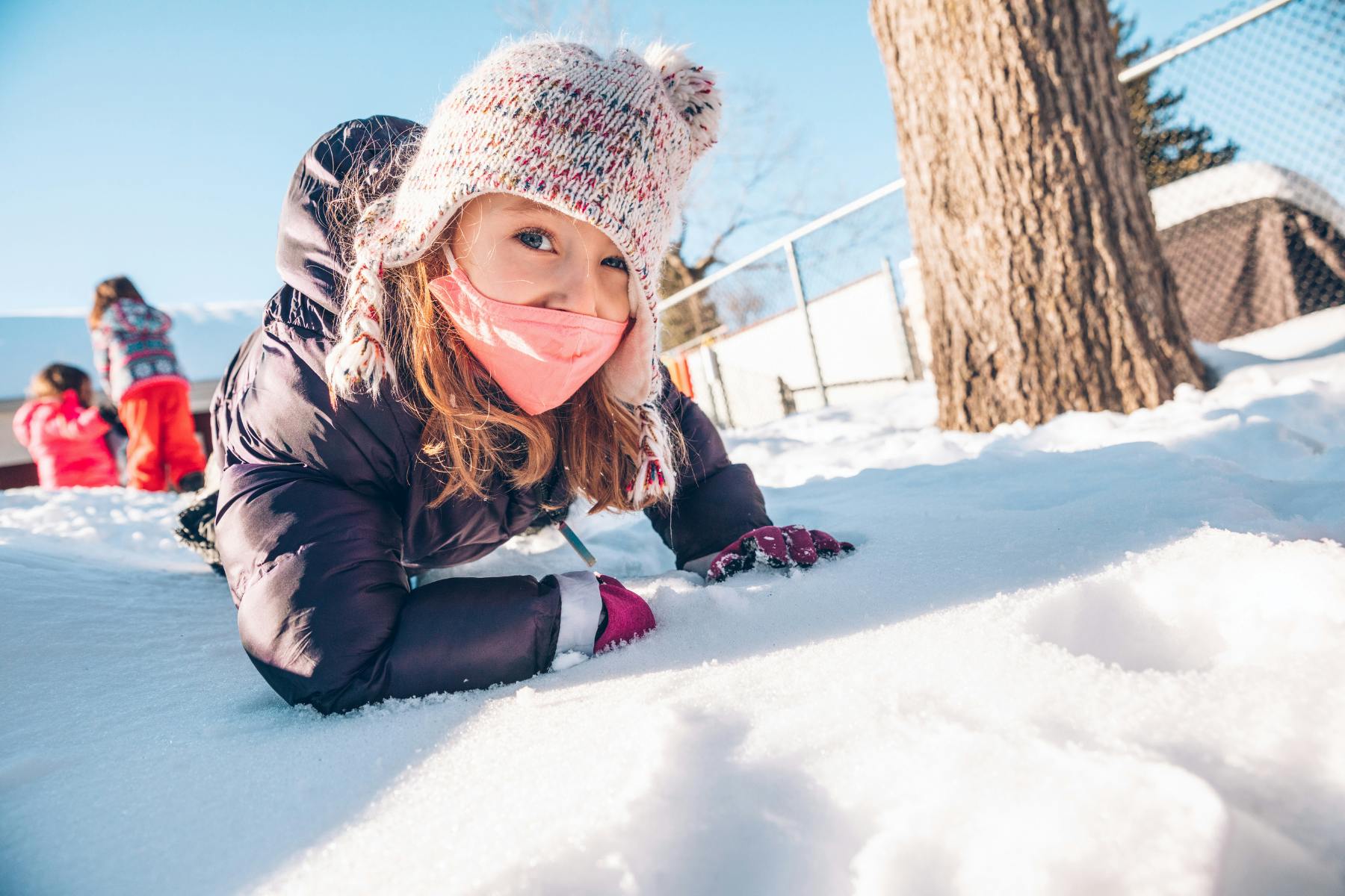 Child in winter clothing and mask crawling in snow