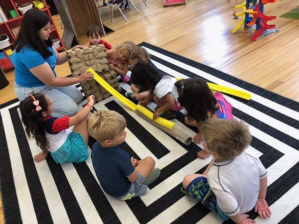 Adult and children playing with a ramp and blocks on a striped rug